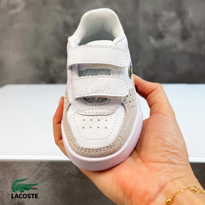 Ténis branco com velcro e logo Lacoste segurado numa mão