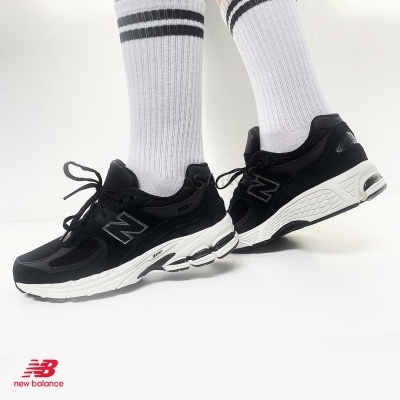 Ténis New Balance negros com meias brancas e riscas pretas em fundo branco.