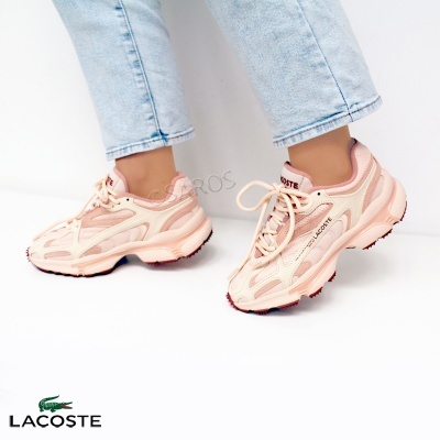 Ténis Lacoste rosa claro com detalhes brancos usados por pessoa com calças de ganga