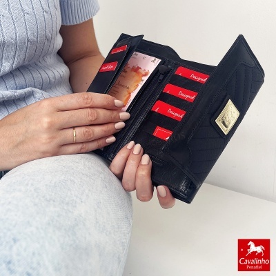 Carteira preta em pele acolchoada com vários cartões vermelhos com texto branco a ser segurada por uma mulher com camisola azul clara e calças cinzentas.