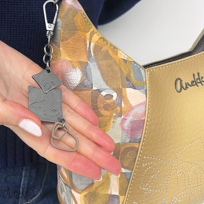 Bolsa de pele sintética com padrão abstrato em castanho, bege, cinzento e rosa e chaveiro metálico prateado com rosto desenhado.