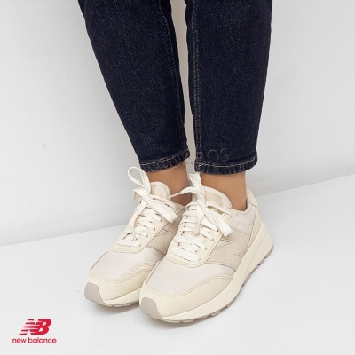 Ténis New Balance bege claro com sola branca usados com calças de ganga escuras