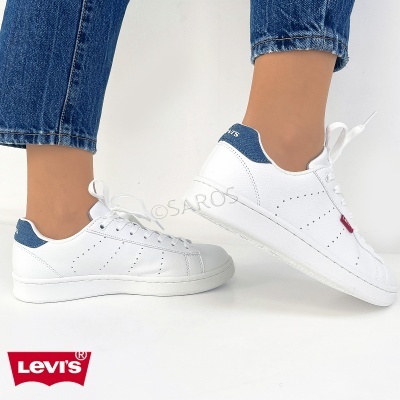 Sapatilhas Levis brancas com detalhes azuis e etiqueta vermelha, usadas com jeans azul