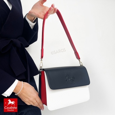 Mala Cavalinho em pele com preto, branco e vermelho apoiada na mão de uma pessoa.