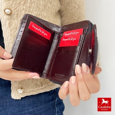 Carteira de pele castanha escura aberta, mostrando compartimentos, segurada por pessoa com casaco bege e jeans