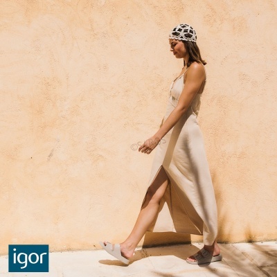 Mulher com vestido longo bege e lenço na cabeça a andar junto a parede clara