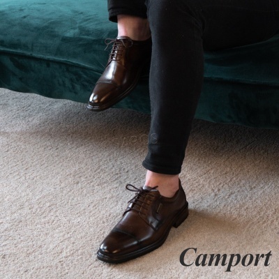 Sapatos sociais castanhos escuros em couro em cima de tapete bege junto a sofá verde