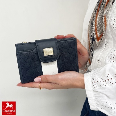 Carteira preta Cavalinho com faixa branca e logo dourado, segurada por mãos femininas.