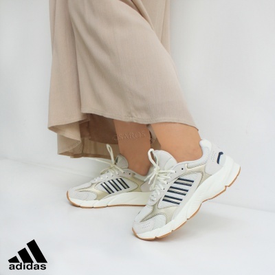 Ténis Adidas brancos com detalhes azuis e sola castanha usados com calças bege claras