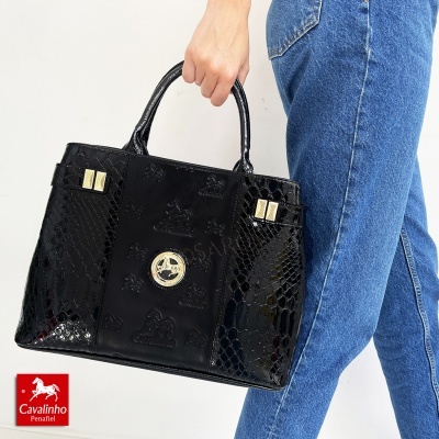 Mala preta Cavalinho Penafiel com detalhes dourados e textura mista, segurada por uma pessoa com calças de ganga azuis