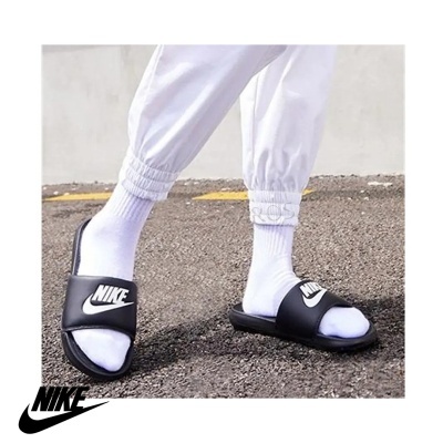 Chinelos pretos NIKE com meias brancas e calças desportivas brancas em piso de asfalto