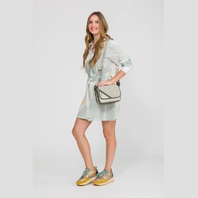 Mulher com vestido verde e bege, sapatos desportivos amarelos e mala castanha Anekke