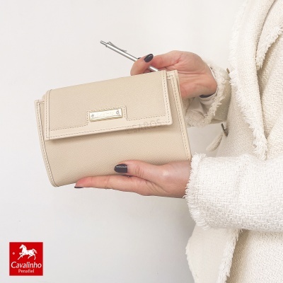 Carteira bege Cavalinho com textura e placa metálica em mão feminina com casaco branco