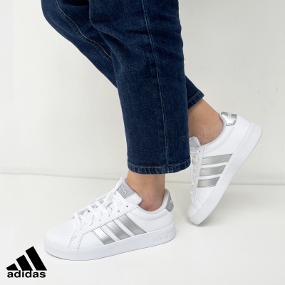 Ténis Adidas brancos com riscas prateadas usados com calças de ganga