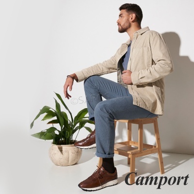 Homem sentado veste roupa casual com sapatilhas castanhas ao lado de vaso com planta