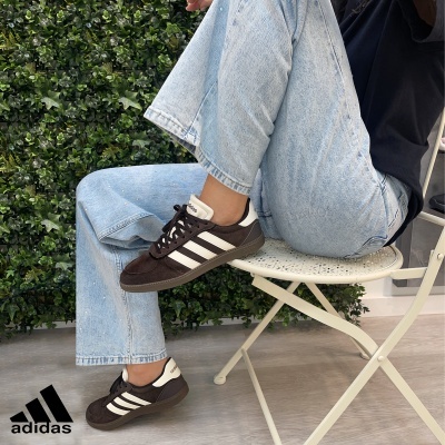 Ténis Adidas castanhos com riscas brancas usados com calças de ganga azul clara e cadeira branca