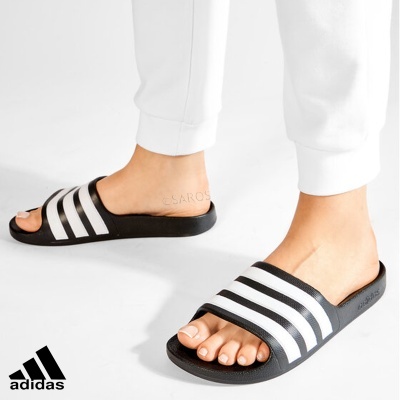 Chinelos Adidas pretos com riscas brancas usados com calças brancas