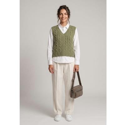 Mulher vestindo camisola de malha verde, camisa branca, calças bege, ténis brancos e bolsa castanha