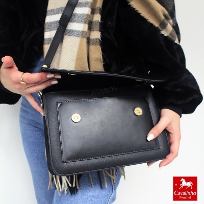 Mala preta em pele com botões dourados e pessoa com casaco preto, jeans e cachecol às riscas