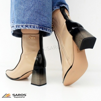 Botas femininas bege com salto grosso preto e bege usadas com jeans azul claro.