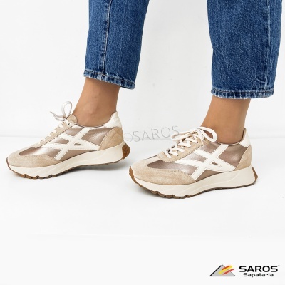 Sapatilhas bege com detalhes brancos usadas por pessoa com calças de ganga azul sobre fundo branco.