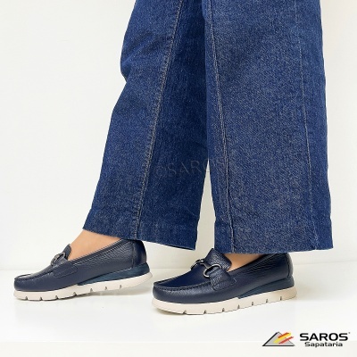 Sapatos mocassim de pele preta com sola branca usados com calças de ganga largas.