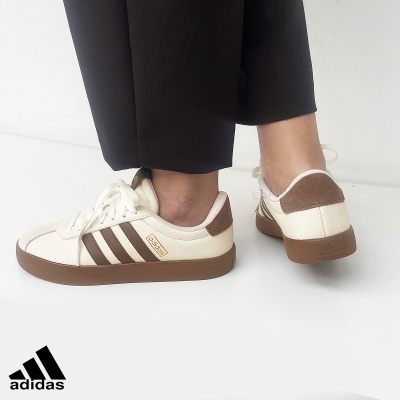 Sapatilhas Adidas brancas com riscas marrons e sola castanha, usadas com calças pretas