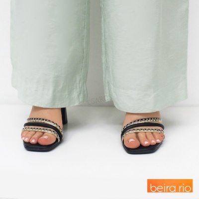 Sandálias de salto com tiras pretas e corrente dourada usadas com calças claras