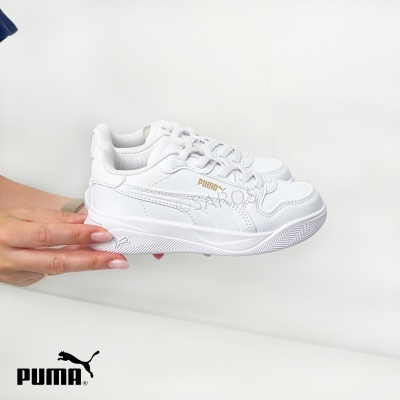Sapatilhas desportivas brancas Puma com logótipo dourado seguradas por mãos femininas