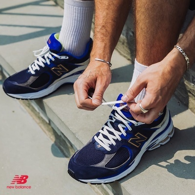 Ténis New Balance azuis escuros com atacadores brancos a serem amarrados