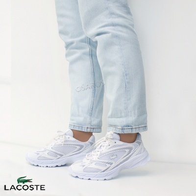 Ténis brancos Lacoste com detalhes cinzentos usados com calças de ganga azul clara