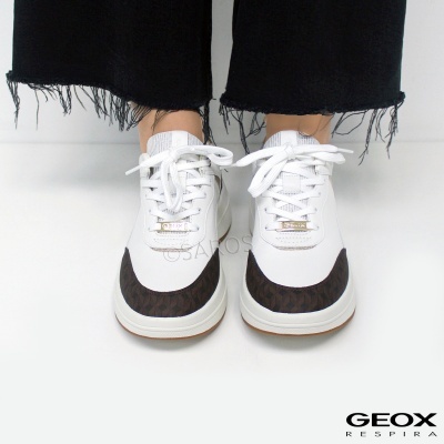 Ténis brancos com detalhes castanho-escuros e padrão texturizado, com atilhos brancos, usados com calças pretas de bainha desfiada