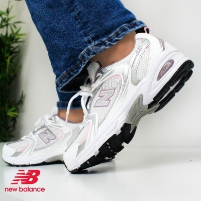 Ténis desportivos New Balance brancos com detalhes cinza e rosa usados com calças de ganga azuis.