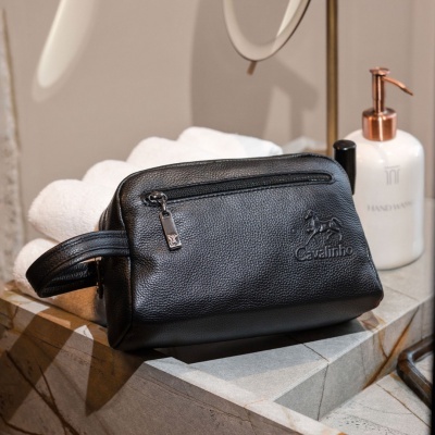 Necessaire preta em pele texturada com fecho e logo Cavalinho sobre lavatório de mármore com toalhas e doseador de sabonete