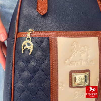 Mala Cavalinho azul escuro e bege com detalhes castanhos e pendente dourado.