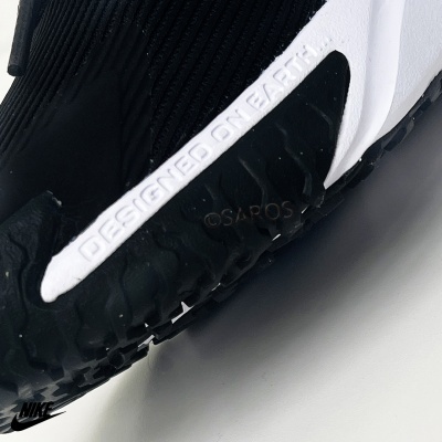 Detalhe de ténis desportivo preto com inscrição 'DESIGNED ON EARTH' em branco na sola.