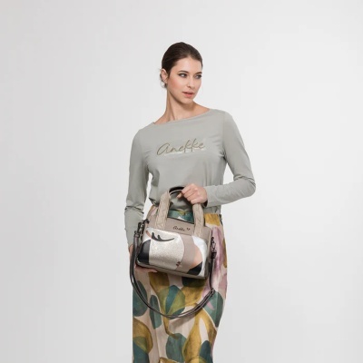 Mulher com roupa cinza claro e saia colorida segurando mala bege com padrão artístico