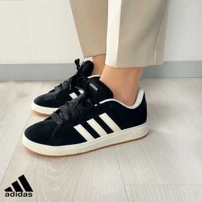 Ténis Adidas pretos com riscas brancas e sola branca num chão de madeira clara