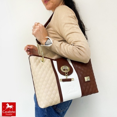 Mala Cavalinho bicolor com alças douradas e mulher a usá-la