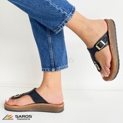 Chinelos pretos com fivela dourada e sola castanha usados com calças de ganga azuis