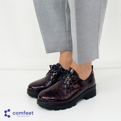 Sapatos oxford em pele verniz castanho escuro com padrão crocodilo e sola preta, usados com calças cinzentas.