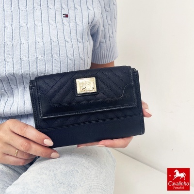 Mala de senhora preta Cavalinho com fecho dourado em padrão diagonal segurada por pessoa com camisola azul clara e calças cinzentas