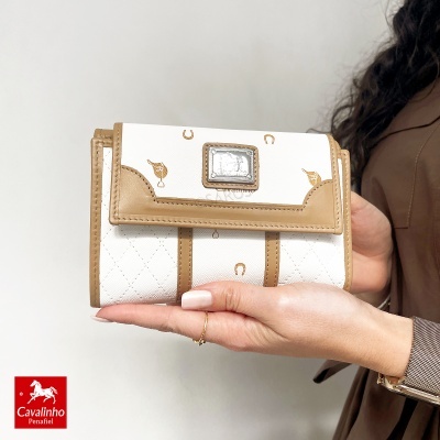 Carteira branca com detalhes em camel e placa metálica Cavalinho nas mãos de uma mulher.