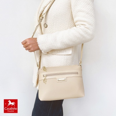 Mala bege claro com fechos dourados e rótulo Cavalinho usada com casaco branco texturizado