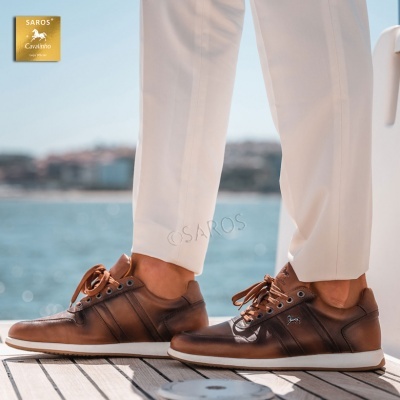 Tênis castanhos com sola branca usados com calças brancas num convés perto da água