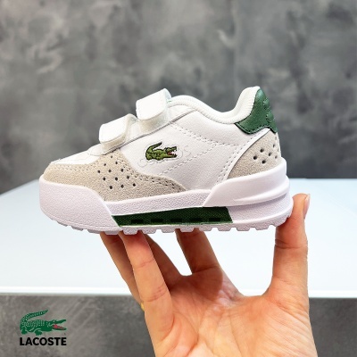 Sapatilha branca de criança com velcro e logo Lacoste verde em fundo cinza