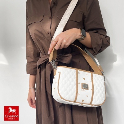 Mala de ombro branca com padrão dourado de cavalos e ferraduras e alças bege e brancas.