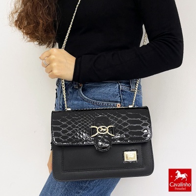 Mala preta com padrão pele e fecho dourado, alça corrente dourada, usada por pessoa com camisa preta e jeans azuis