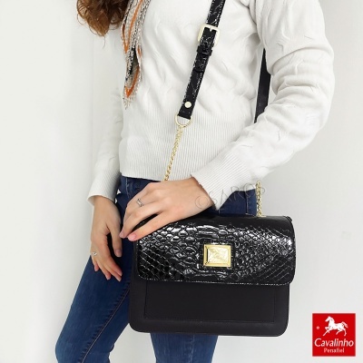 Mala preta Cavalinho com textura de pele de cobra e alça preta, usada por mulher