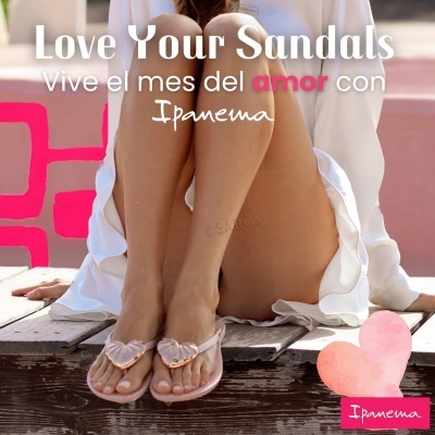 Sandálias rosa claro com coração translúcido em mulher com vestido branco sentado em madeira